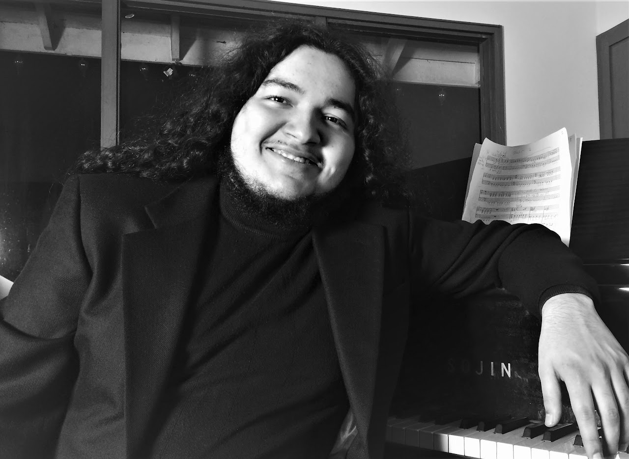 Alex Sanchez seated beside a piano